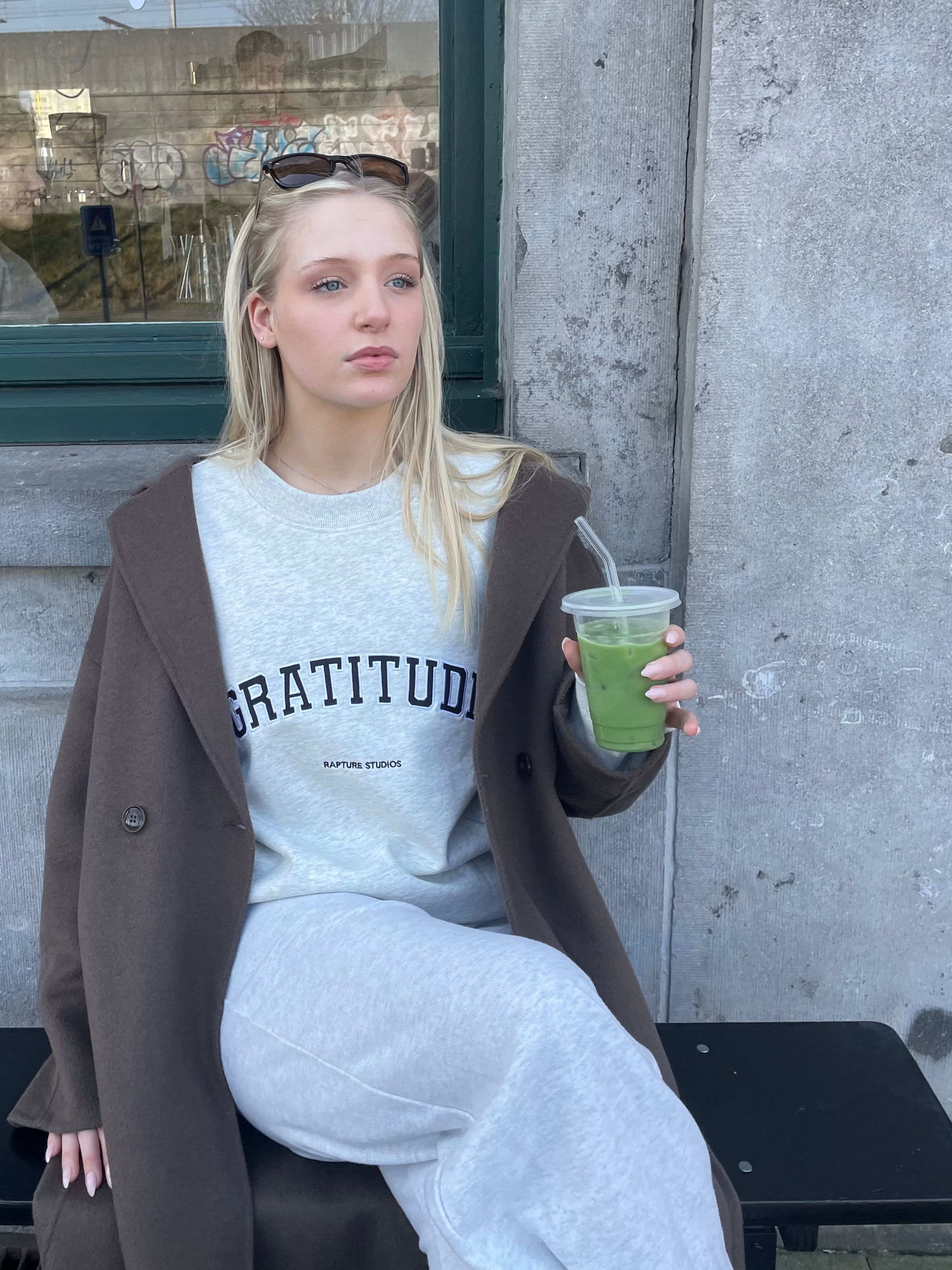 Woman holding a green drink outside a building with a glass door.